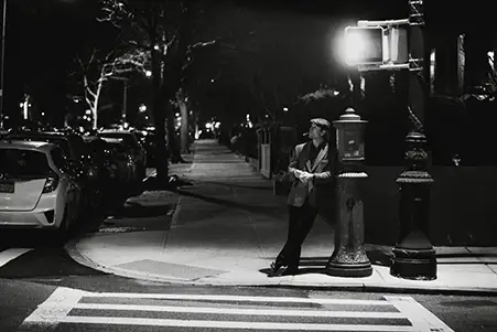 night exterior, a man smoking a cigarette leaning against a lamp post.