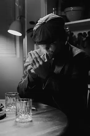 night interior, a man at a table smoking a cigarette.