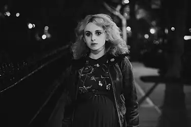 night exterior, a young woman standing in the street.