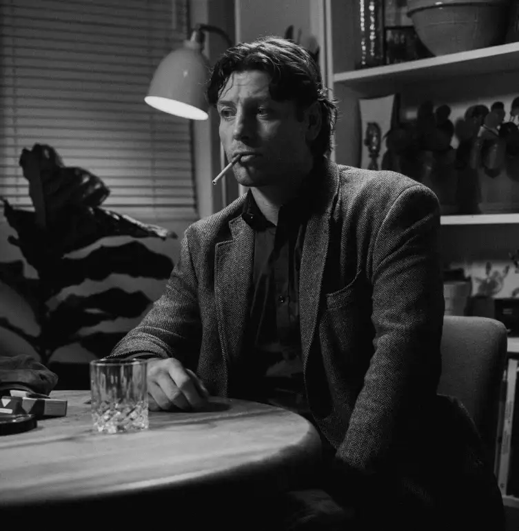 night interior, a man at a table smoking a cigarette.